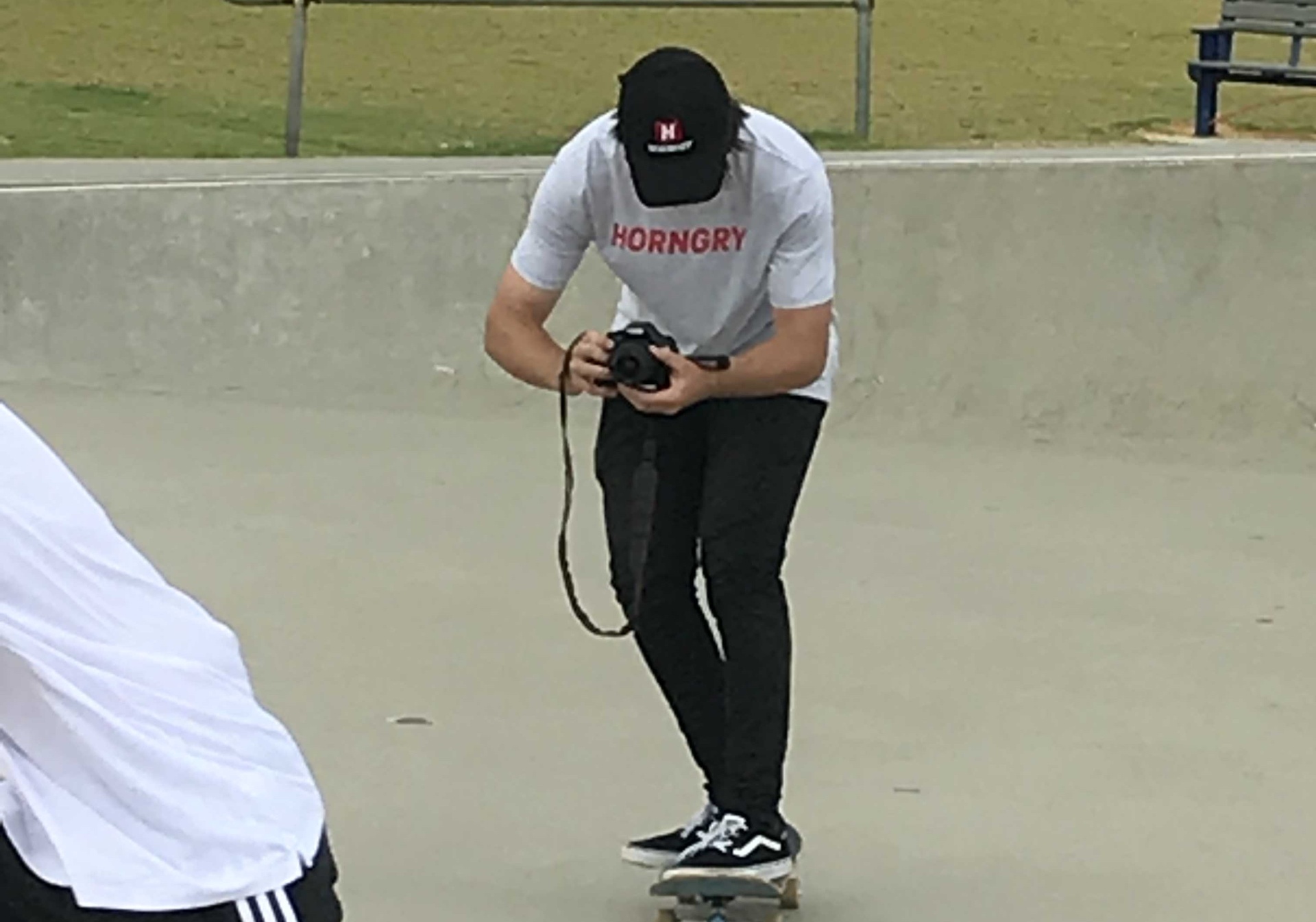 A HORNGRY culture contributor in a branded tee filming a skater with a camera at a skate park